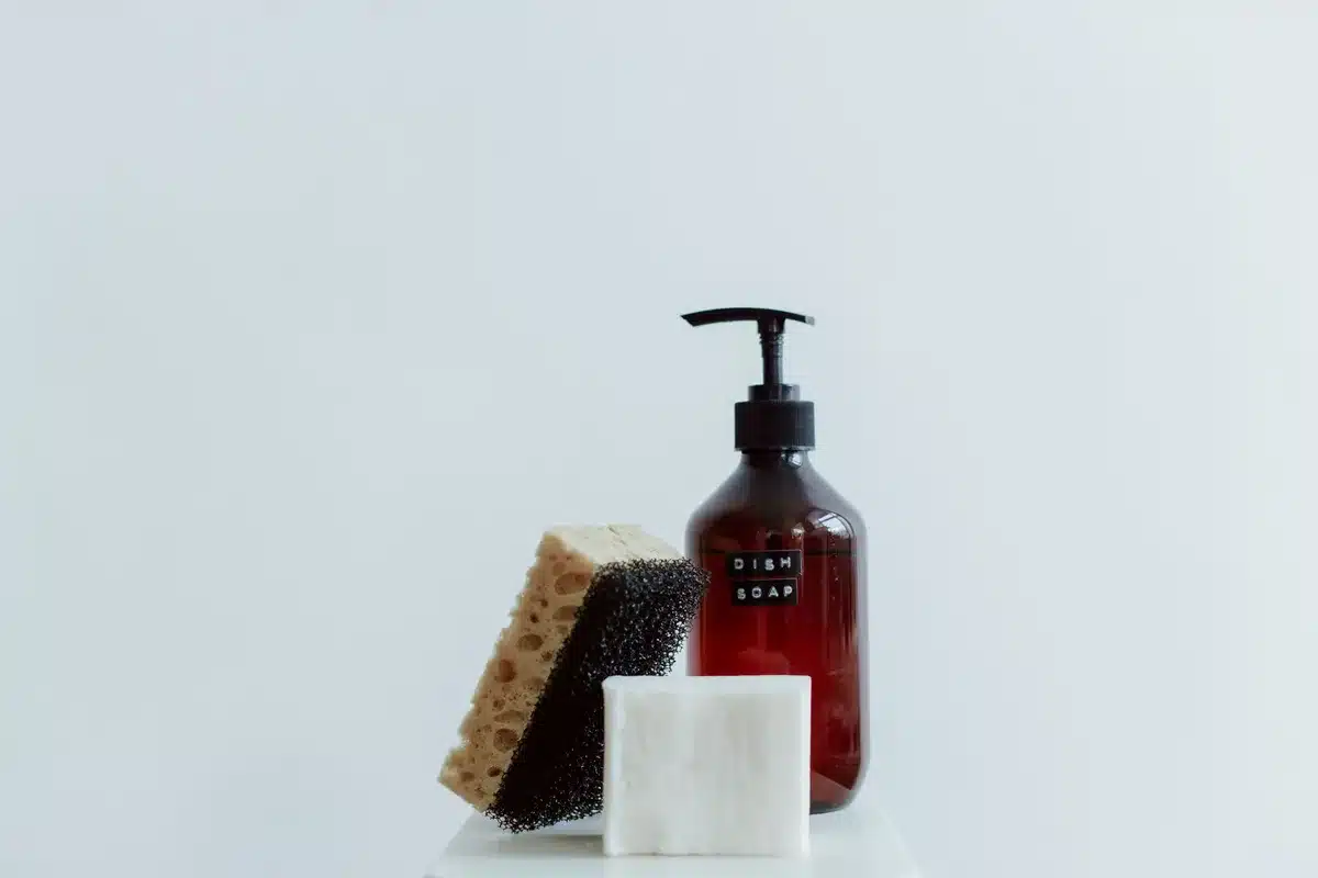 Brosse à vaisselle avec distributeur de savon intégré utilisée pour nettoyer des assiettes dans un évier