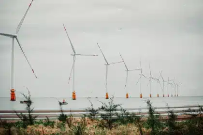 Paysage côtier breton avec plateforme éolienne en mer à l'horizon et bateaux de pêche au premier plan
