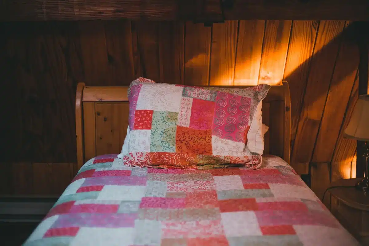 Courtepointe color&eacute;e pos&eacute;e sur un lit avec un coussin et une lumi&egrave;re douce