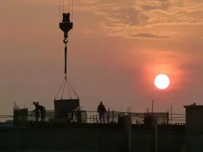 Silhouettes anonymes devant un grand chantier industriel avec grues et tuyaux au crépuscule