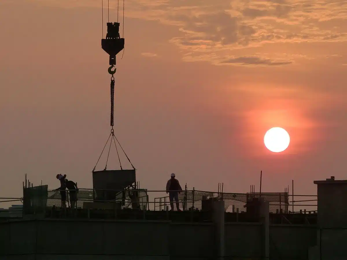 Silhouettes anonymes devant un grand chantier industriel avec grues et tuyaux au crépuscule