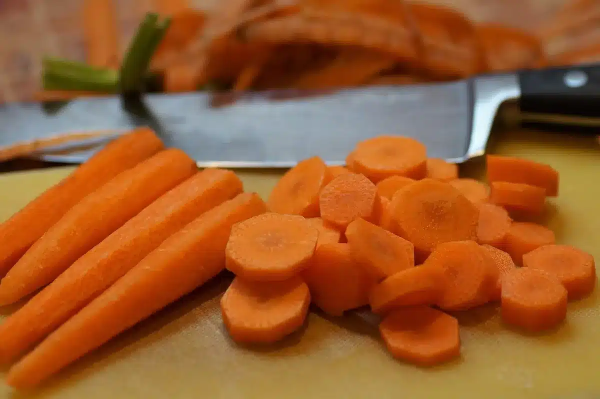 Patates douces et carotte pelées sur une planche prêtes à être coupées